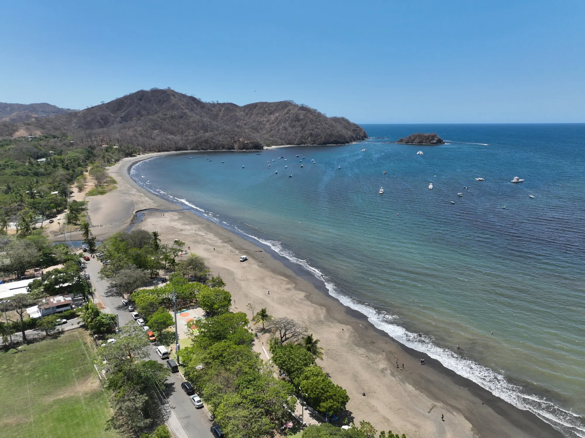Aerial view of the curved beach and bay at Playas del Coco, with forested hills behind